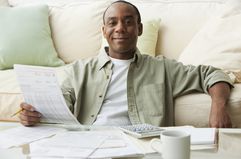 A man paying bills at his coffee table with papers, a calculator, and a coffee mug on the table