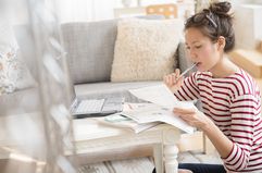 Woman looking at paperwork with a laptop at home