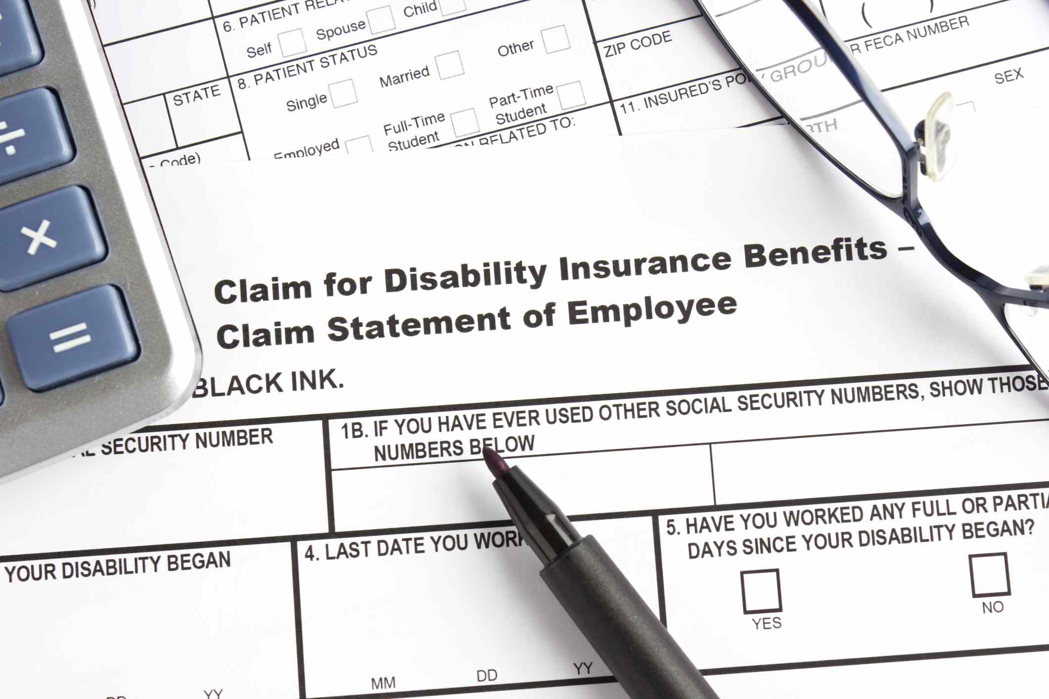 A disability insurance claim form with pen, calculator, and eyeglasses.