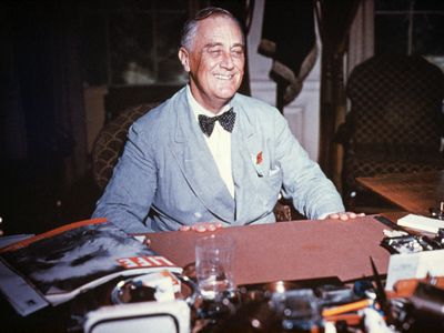 Portrait of Franklin Delano Roosevelt seated at his desk, smiling. Undated color slide.