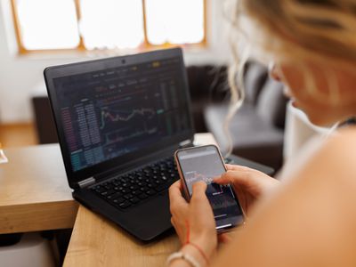 Woman looking at a mobile device and an open laptop