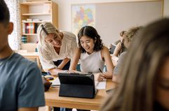 Smiling teacher helping female student in classroom