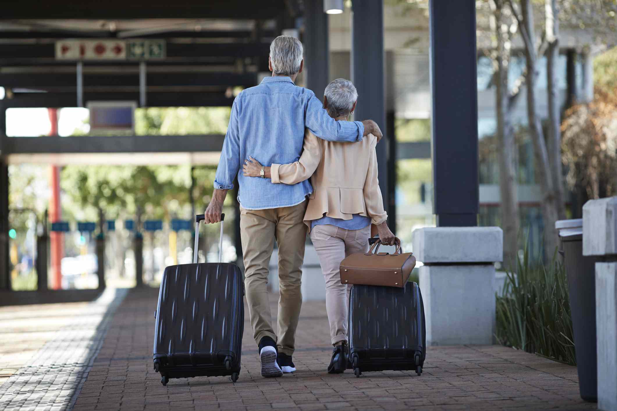 Older couple walking away, each pulling a rolling suitcase