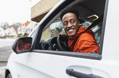 Smiling young driver looking back through window while driving delivery van