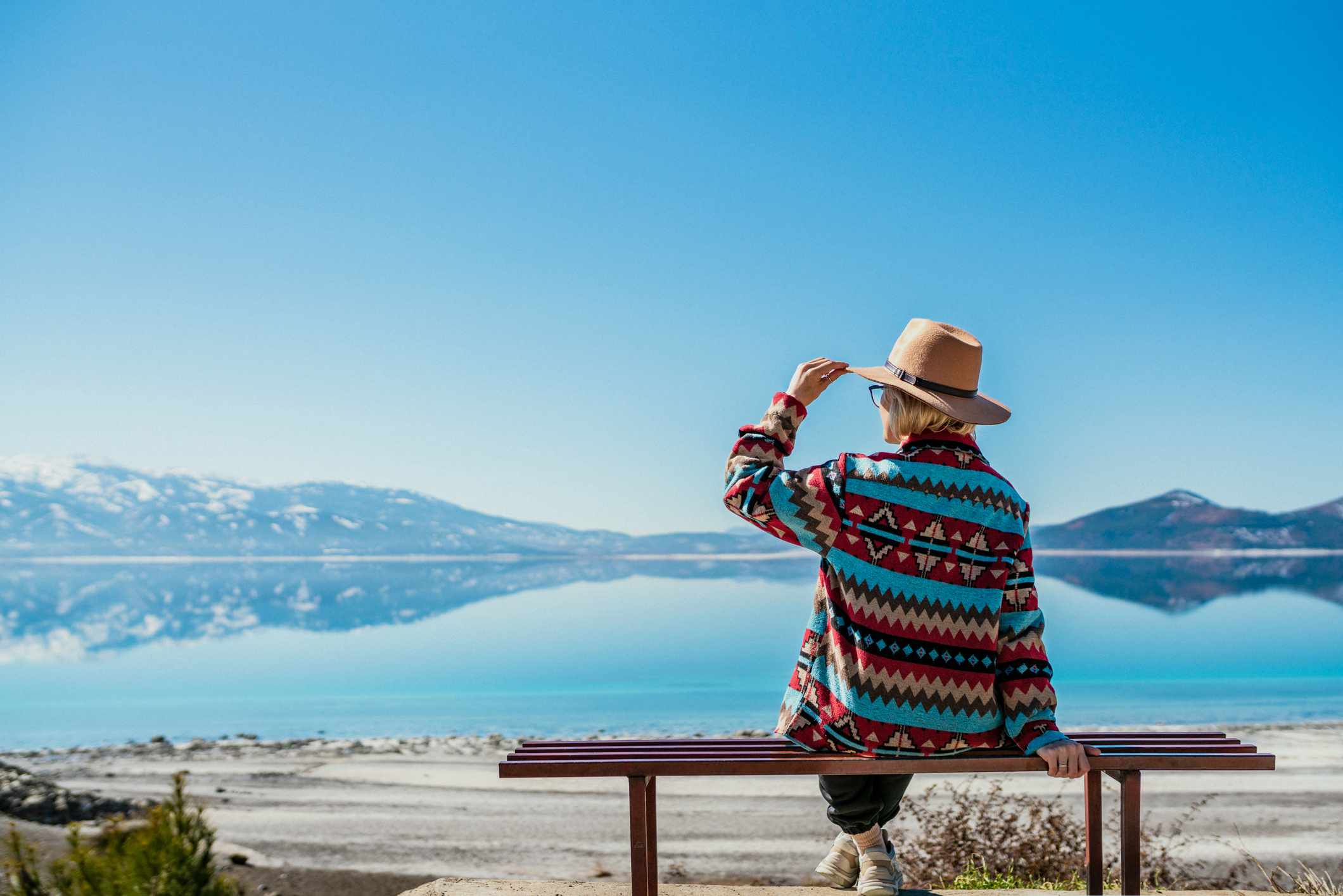 Woman sitting near beautiful blue lake with white sand beach and enjoying its stunning view. Salda Lake, Turkey