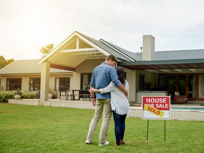 Couple standing next to real estate sold sign at their new house