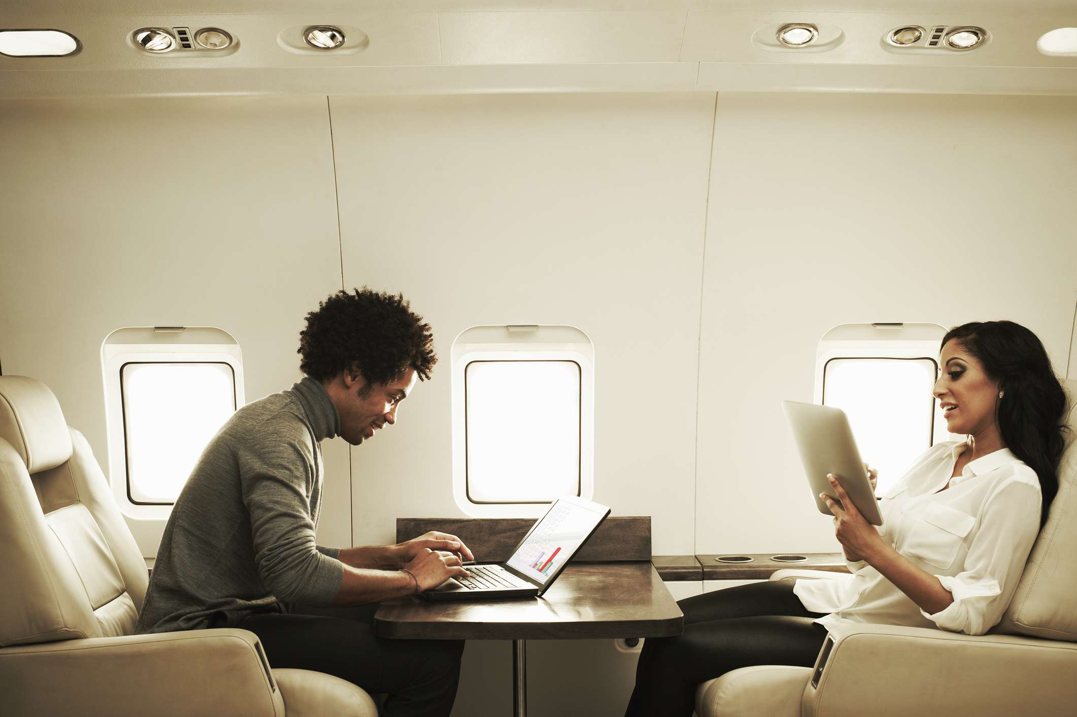 Couple on a private jet using a laptop and tablet