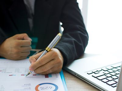 A close-up of a person's hands holding a pen over papers displaying financial data