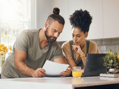 A young couple reviews documents and comparing mortgage rates in a kitchen.