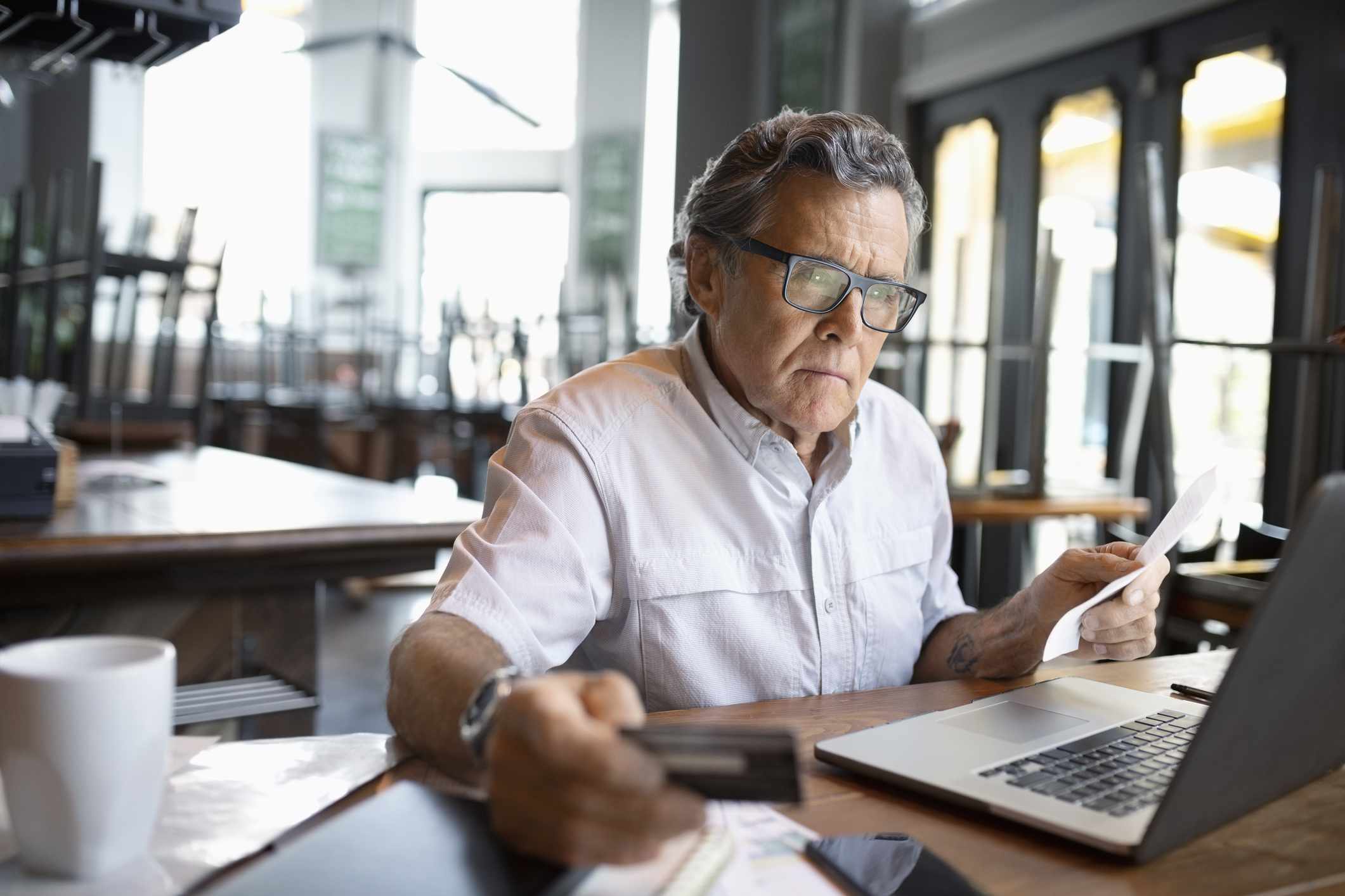 A focused restaurant owner paying bills at laptop.