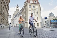 Older couple riding bikes on cobblestone street in Germany