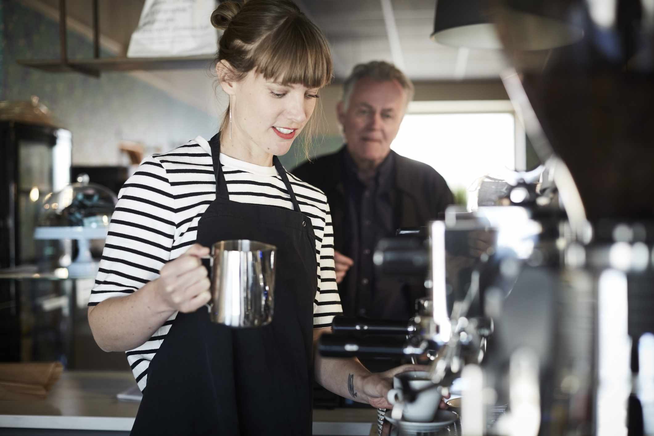 Female barista holding pitcher while making coffee for customer in back