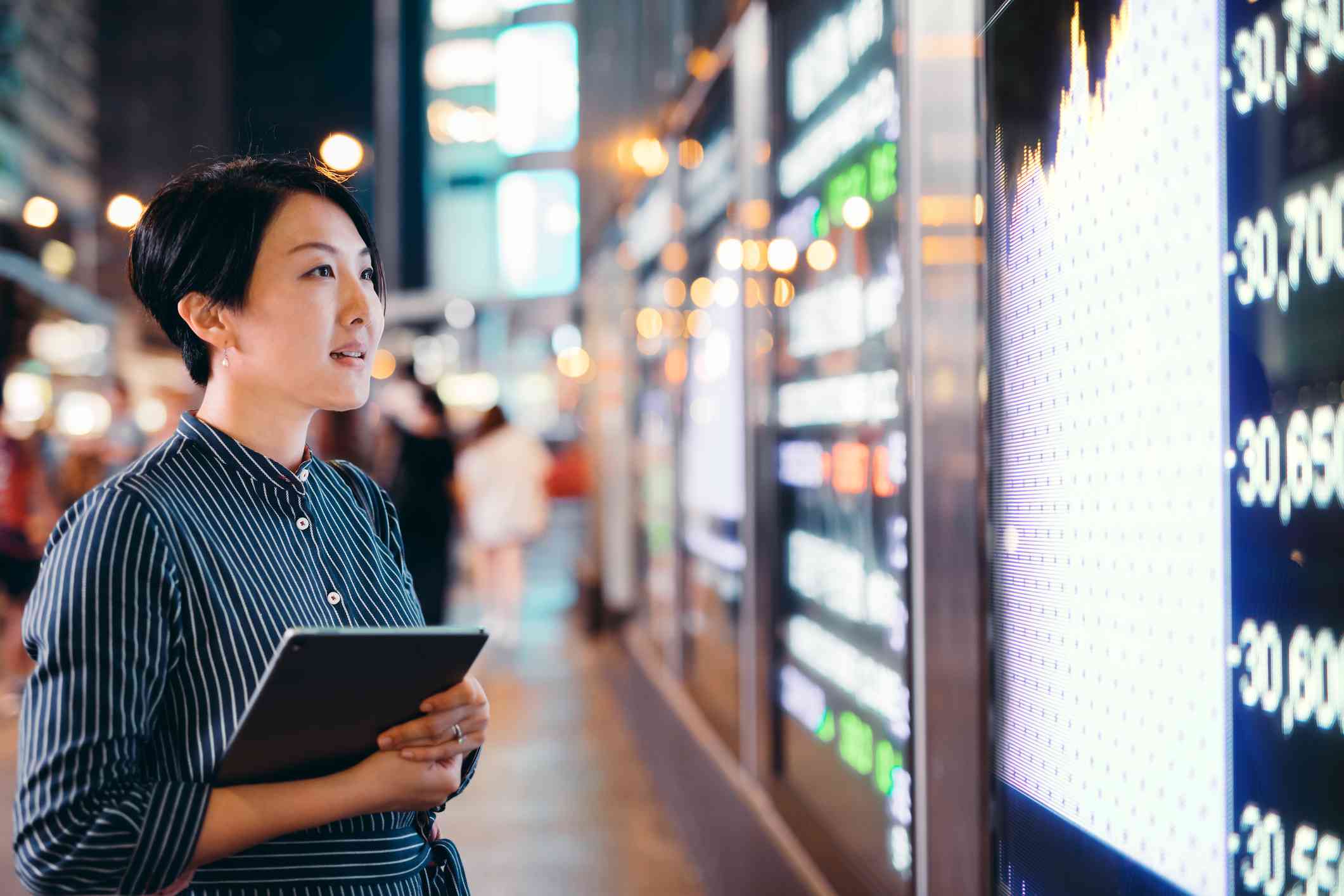 Businesswomen checking stock market data on tablet before Hong Kong financial display board