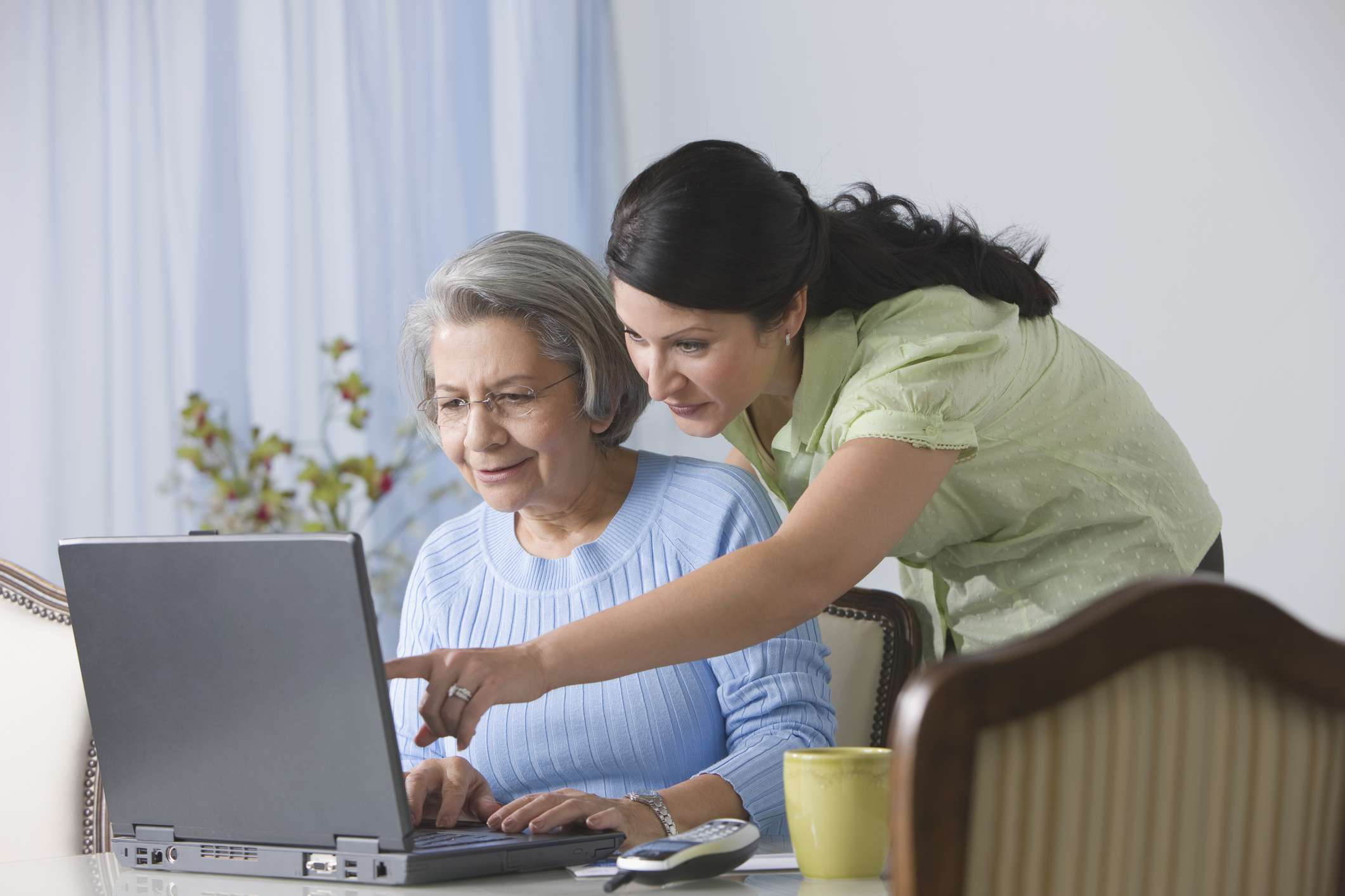 A young woman shows an older woman how to use a laptop.