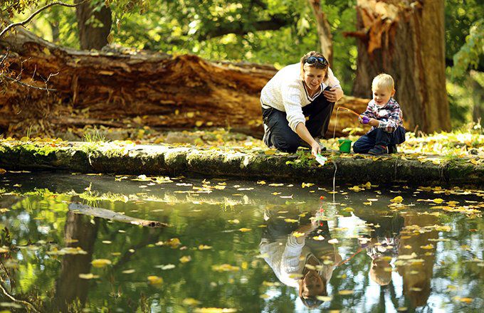 A woman, presumably a mother, teaches her child how to fish in a small forest lake.