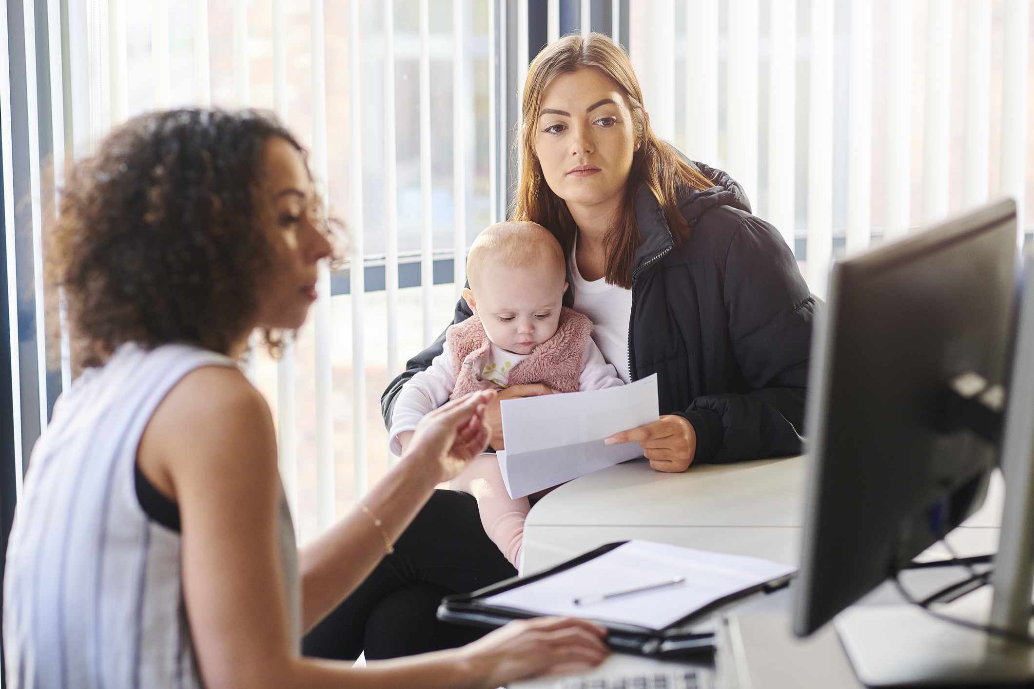 A young mother, with a baby in her lap, getting help from a support worker.