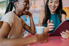 Two young woman having a coffee break and using a digital tablet