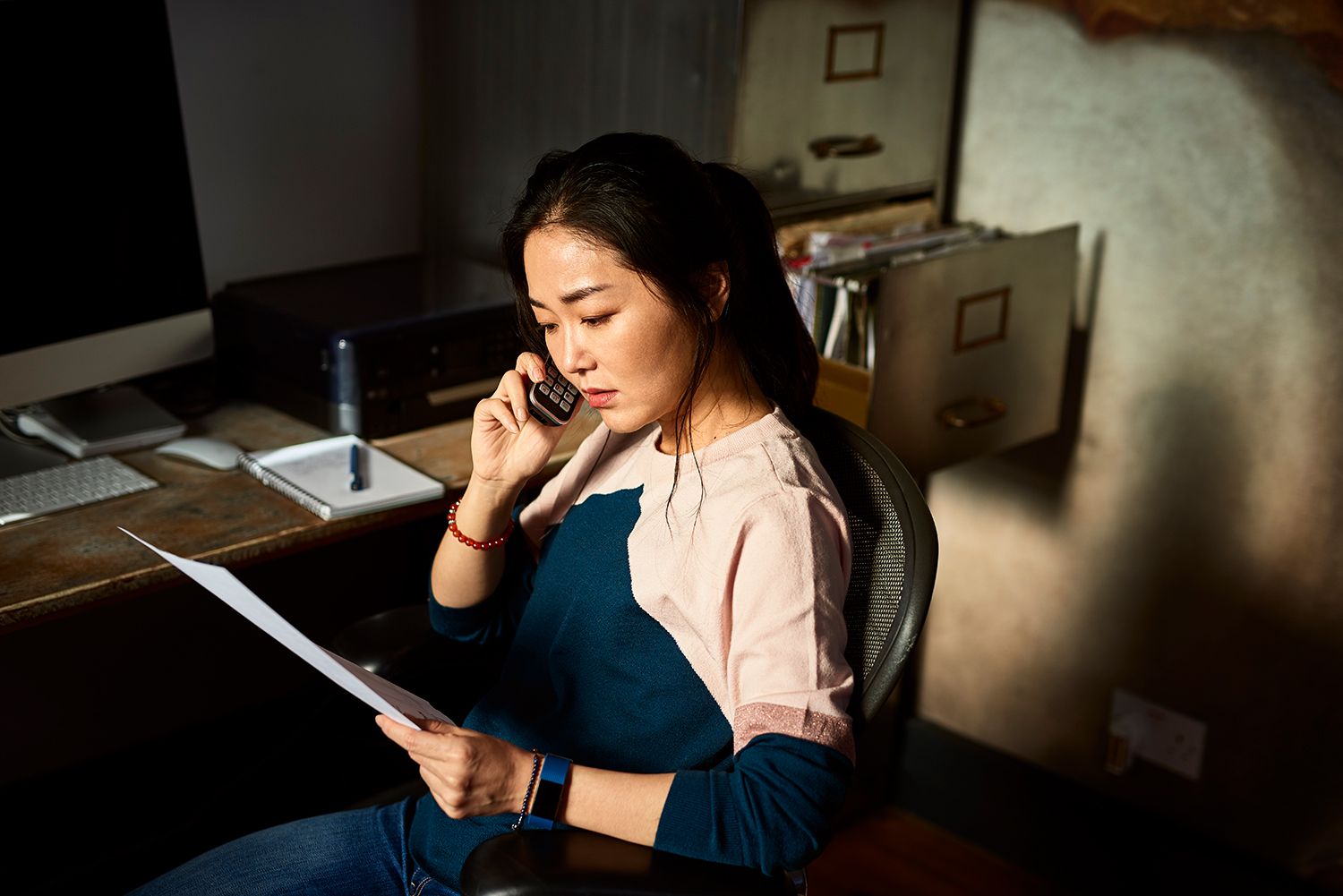 Portrait of Korean woman on cell phone reading important document.