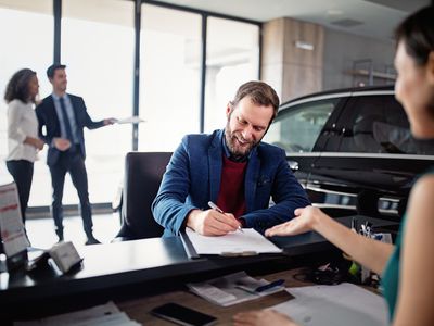 A man signs documents at a car dealership desk to buy a car.