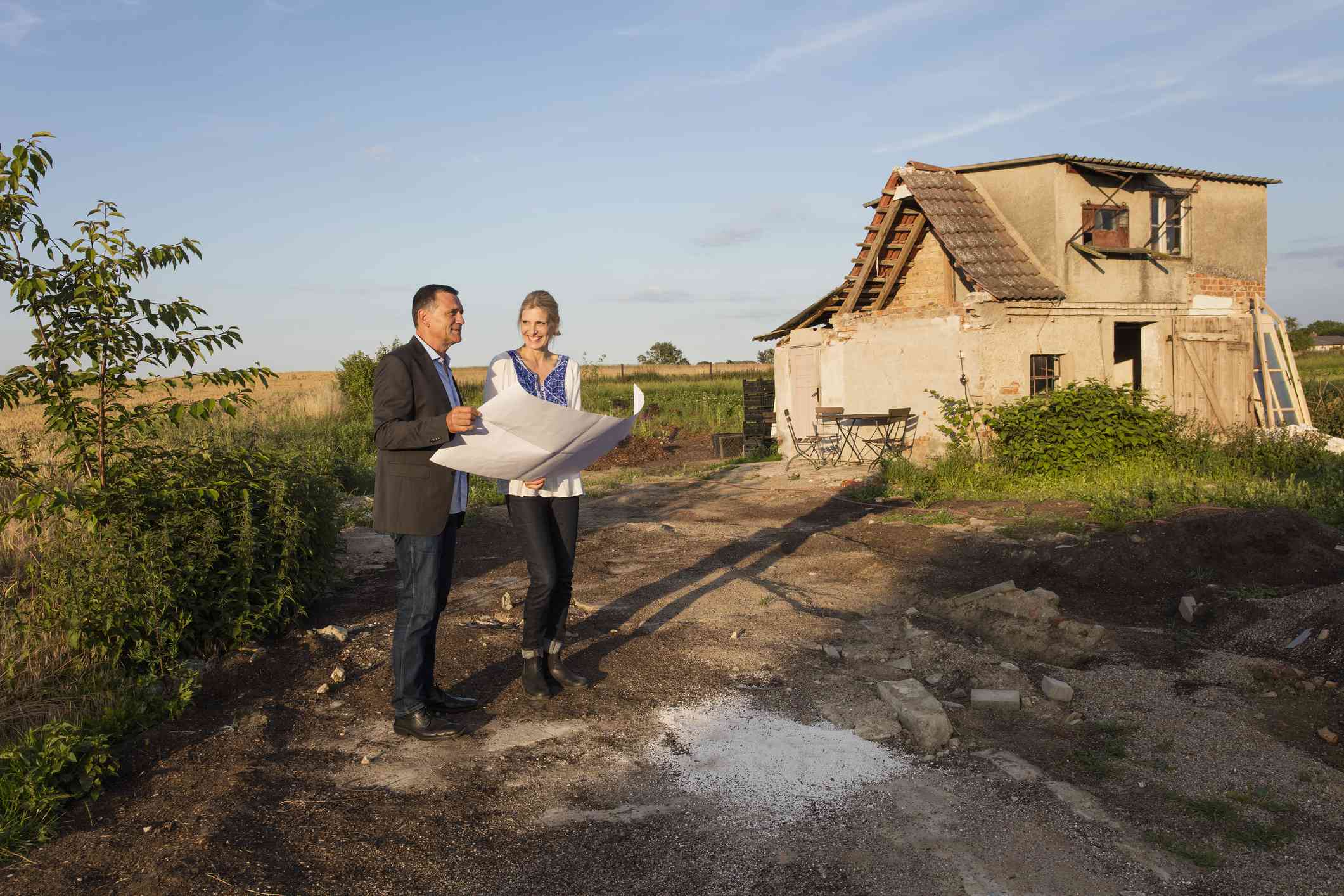 Smiling woman with real estate agent reading document while standing against farmhouse.