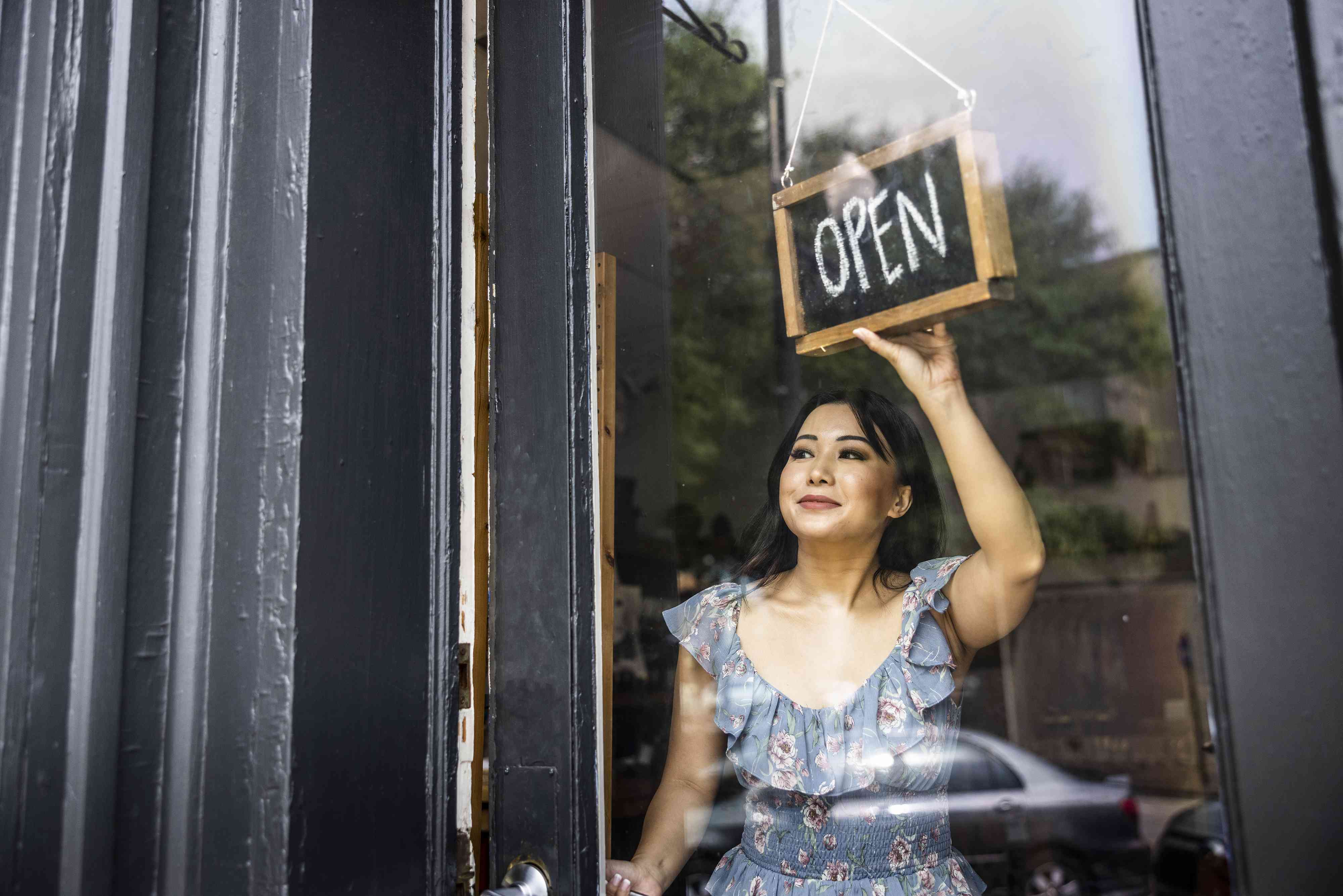 Female small business owner turning “Open” sign in her store