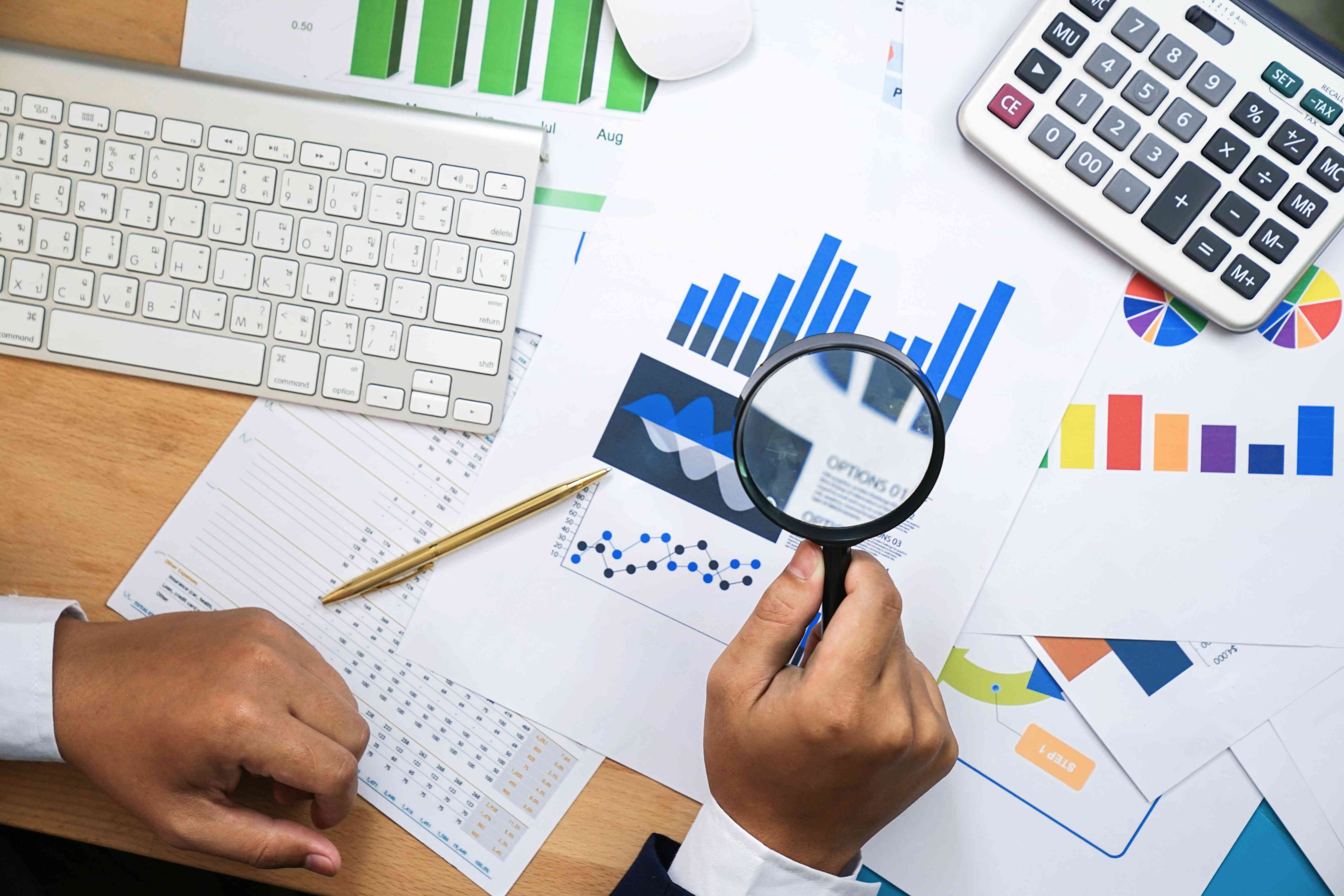 Hand holding a magnifying glass over financial statements