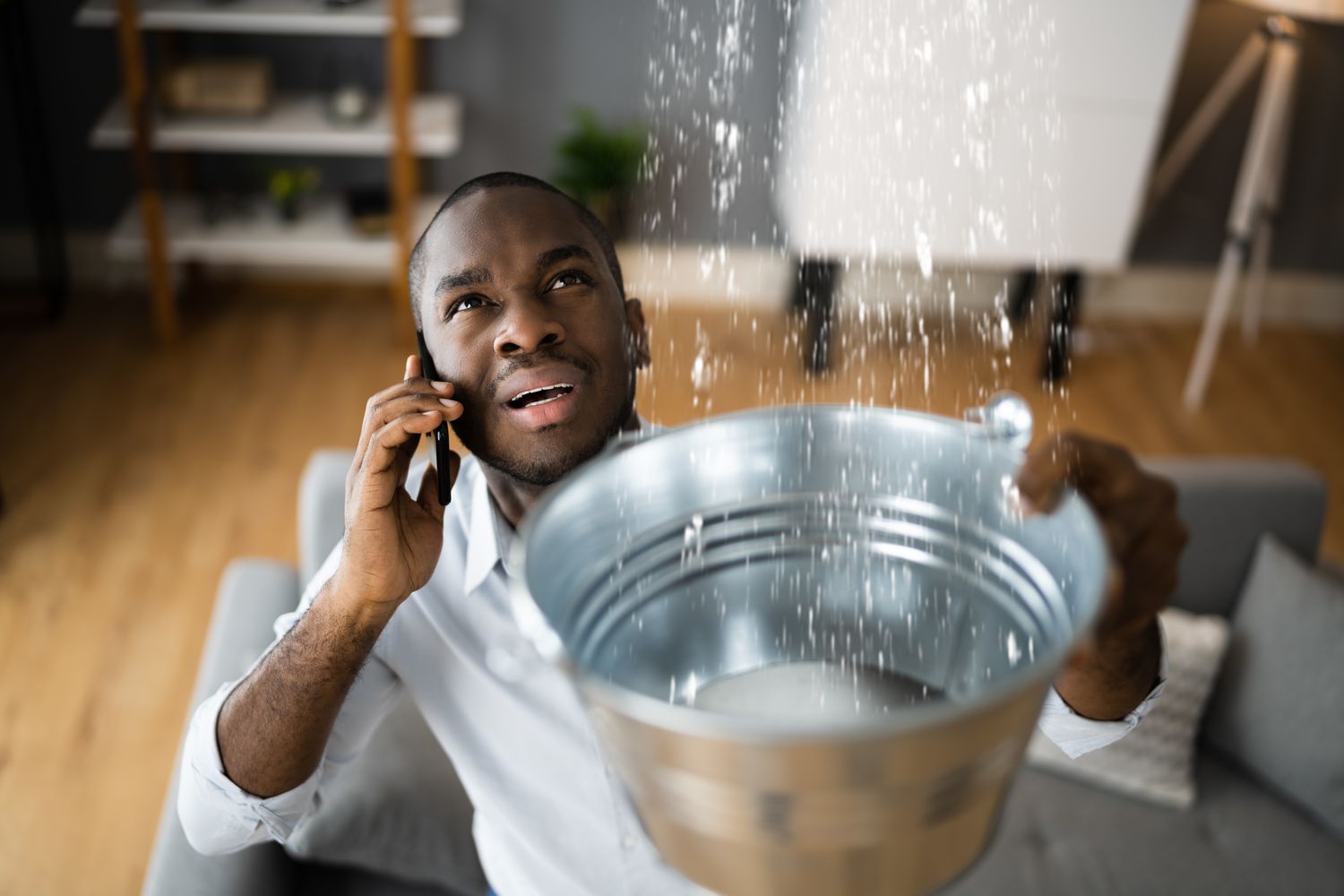 Man on a cellphone holds up a metal pail while water sprinkles from above.