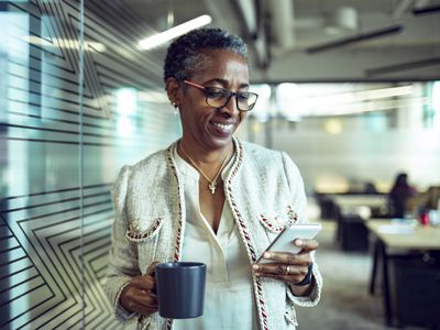 An older employee holds coffee and checks her phone.