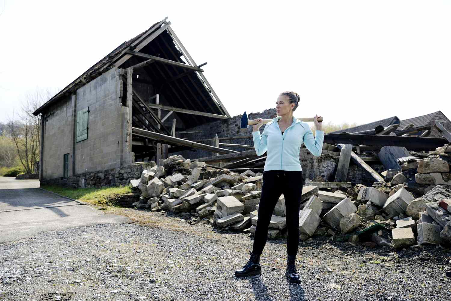Thoughtful woman holds sledge hammer in front of destroyed home