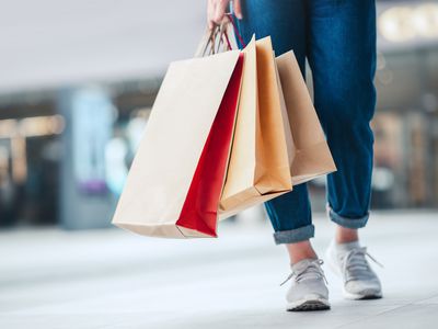 Bottom cropped legs of a person wearing jeans and sneakers and holding three paper shopping bags