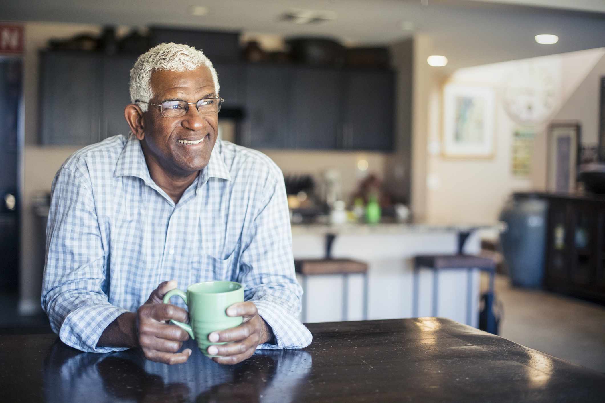 An older man drinks coffee in a kitchen.