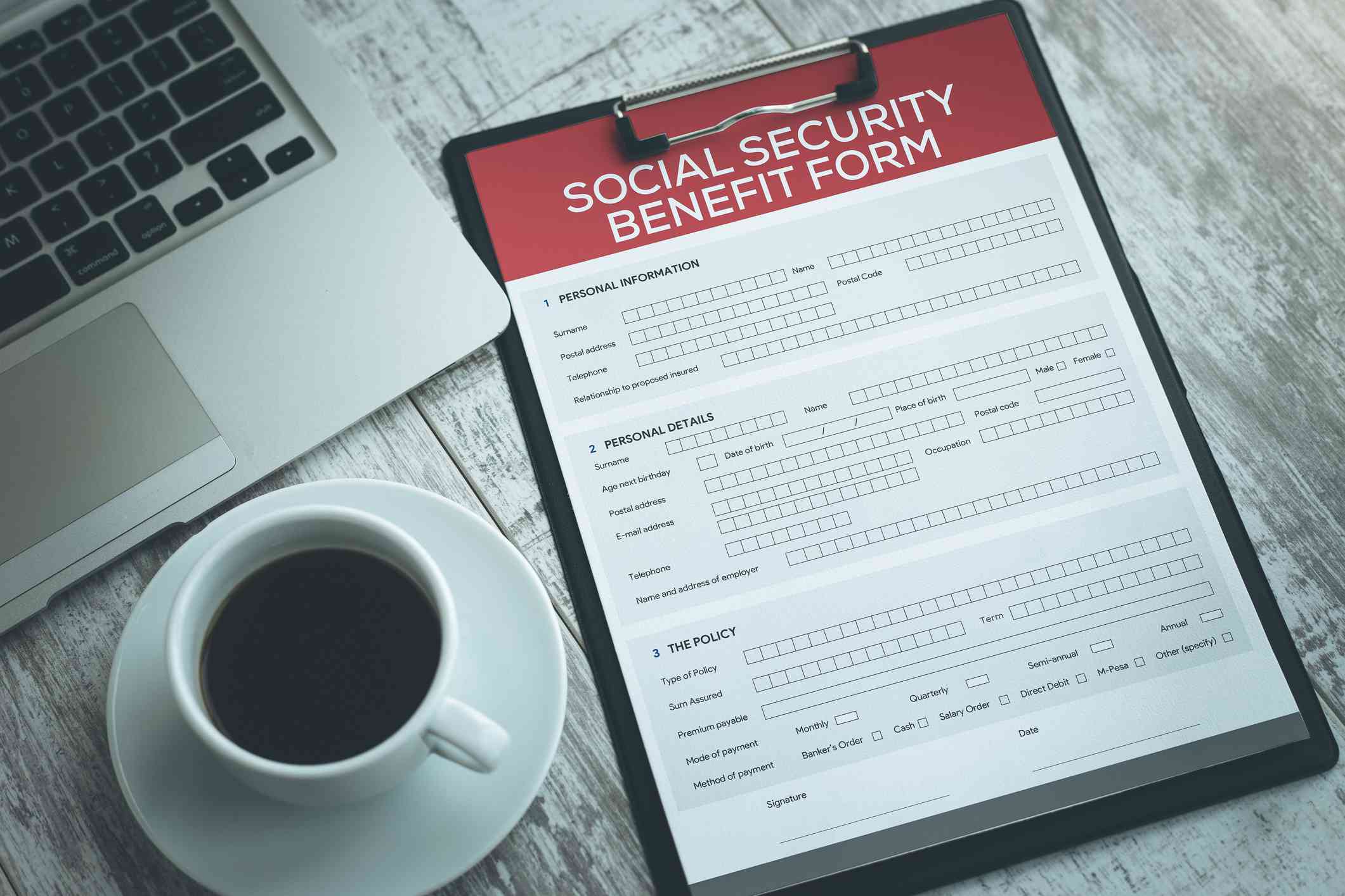 A Social Security benefit form on a desk, with a laptop computer and a cup of coffee.