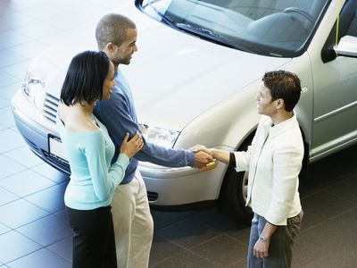 couple shaking hands with a woman after she sells them a car