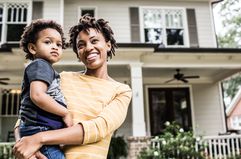 A mother and daughter standing in front of their home. 