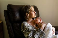 Thoughtful mother looks out the window as she holds her newborn baby