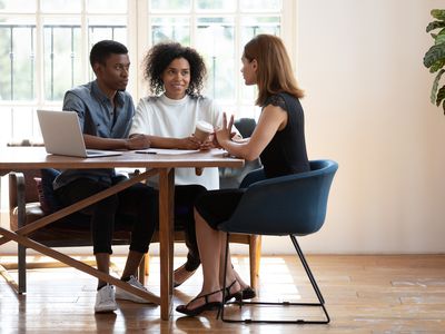 Young couple sits at desk talking with female real estate agent about buying a house