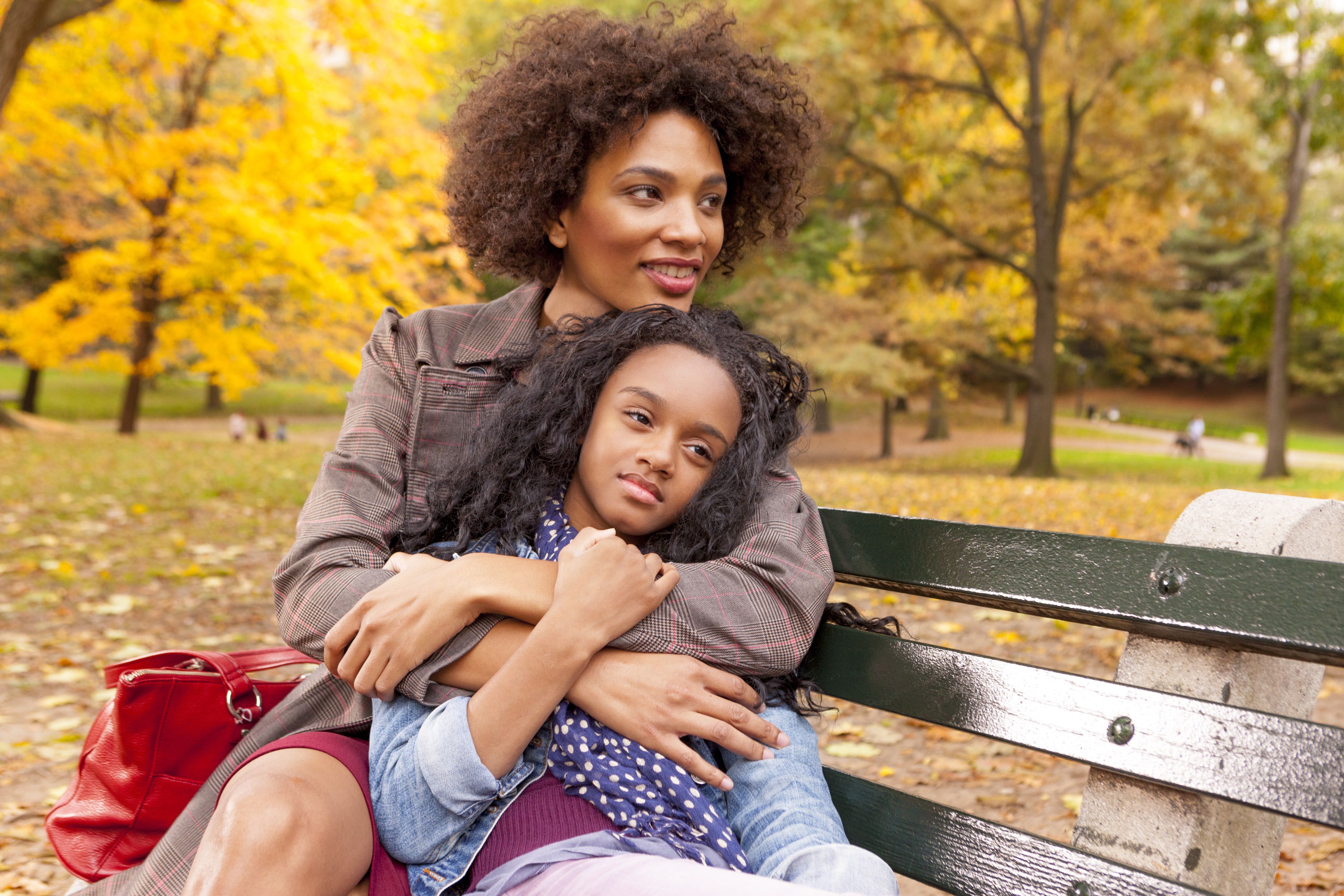 mother and daughter sitting on park bench in fall