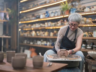 Senior woman artist making clay bowl on a pottery wheel in her studio.