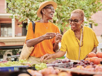 Two mature women shopping at an outdoor food market. 