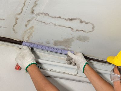 Worker fixing pipe in water-stained ceiling