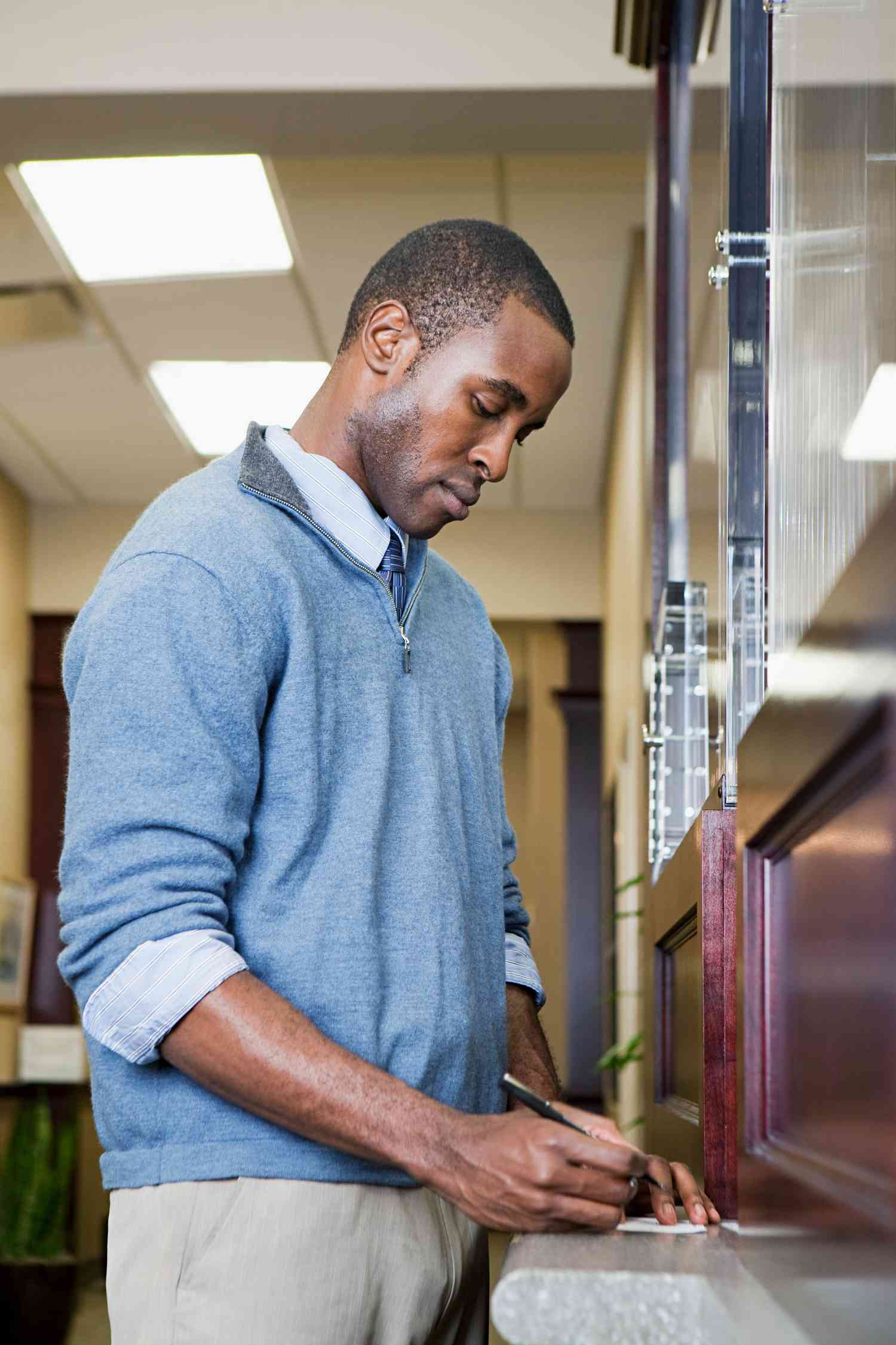 A customer fills out a savings deposit slip at a countertop in a bank.