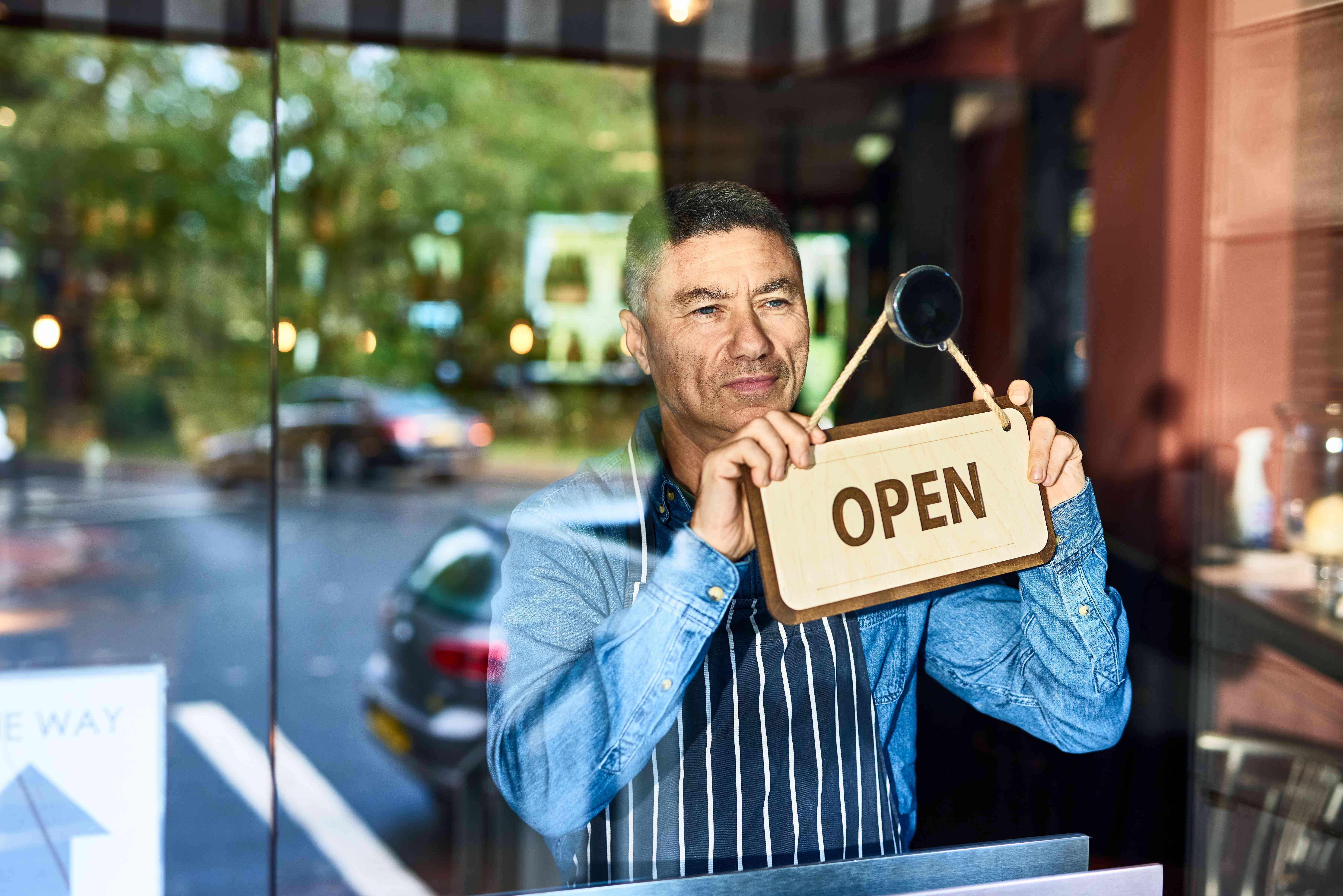 A business owner holds an “Open” sign.