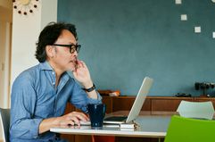 A man sits at a desk on a laptop with a coffee mug