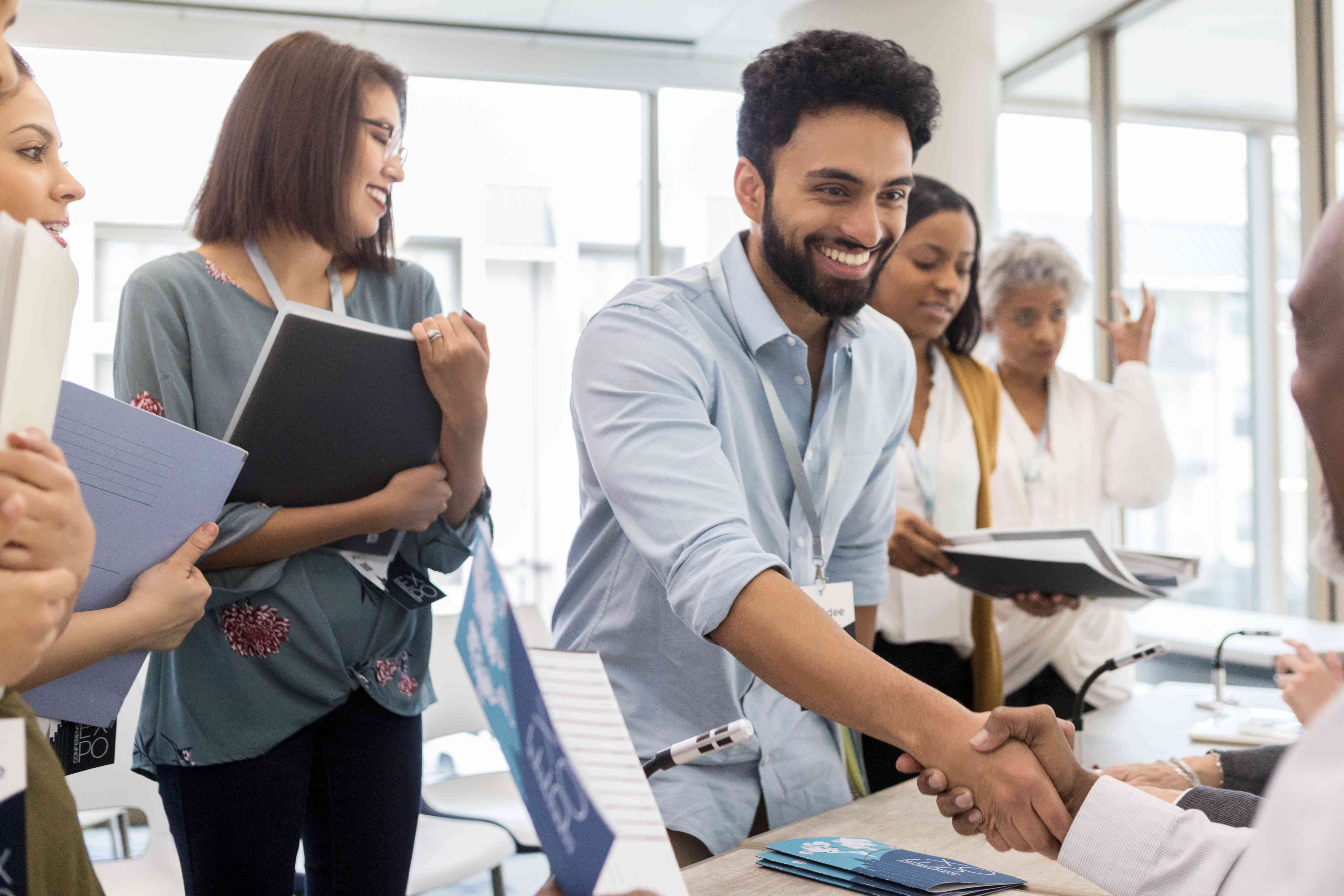 Professional Middle Eastern man, surrounded by other people with folders, shaking hands with someone at desk