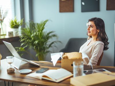 Woman sitting in modern office with book, computer, and boxes around her