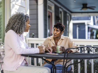 Two women have coffee on a home porch.