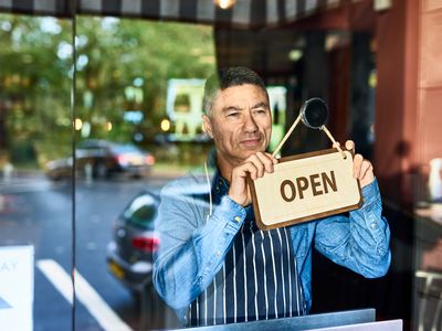 A business owner holds an “Open” sign.