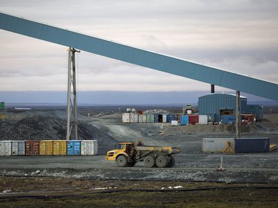 A truck at a mining site passes by a large conveyor machine transporting rock containing gold to a processing plant. 