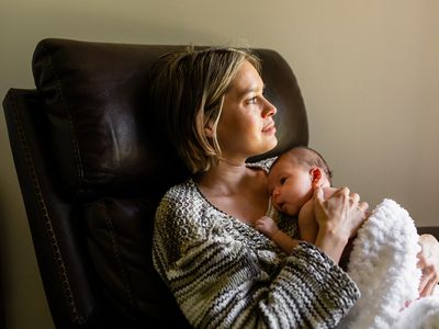 Thoughtful mother looks out the window as she holds her newborn baby