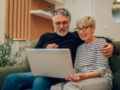 Older couple sitting on their couch and looking happily at something on their laptop screen